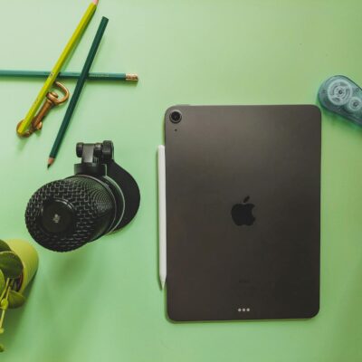 Flat lay of a workspace featuring a tablet, microphone, and stationery on a green desk.