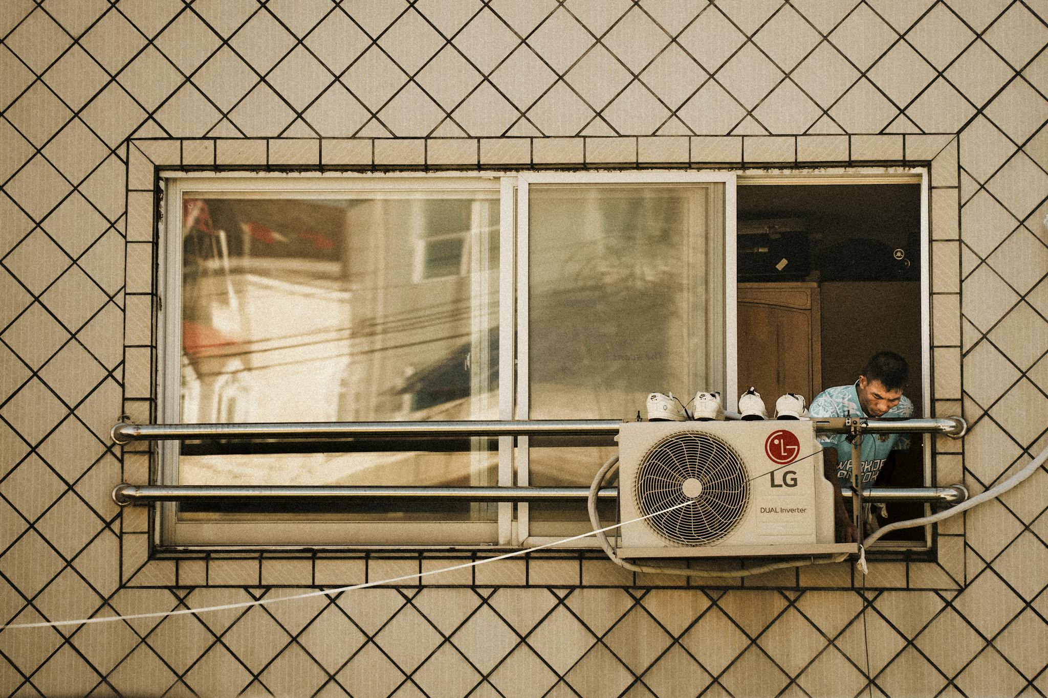 Man looks outside a window with an LG air conditioner unit visible, creating a reflective effect.