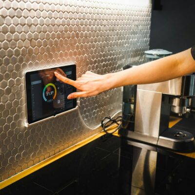 Modern kitchen scene featuring a hand using a tablet to control a smart home system.